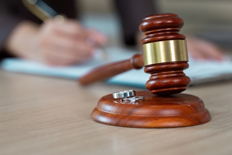 A gavel and wedding rings on a desk as a lawyer prepares divorce documents