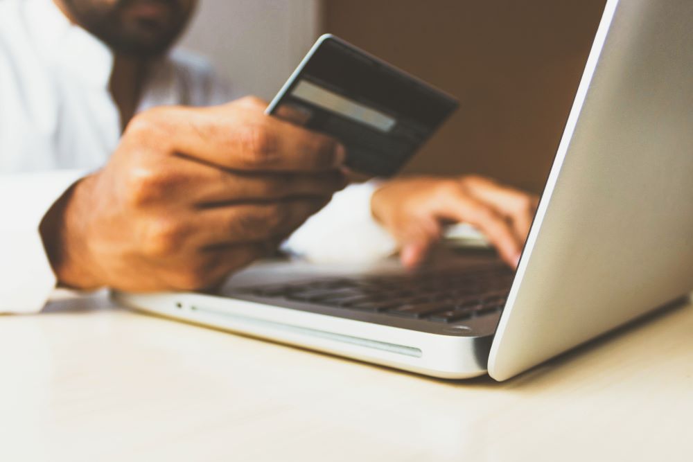 Man holding a credit card while typing on a laptop.